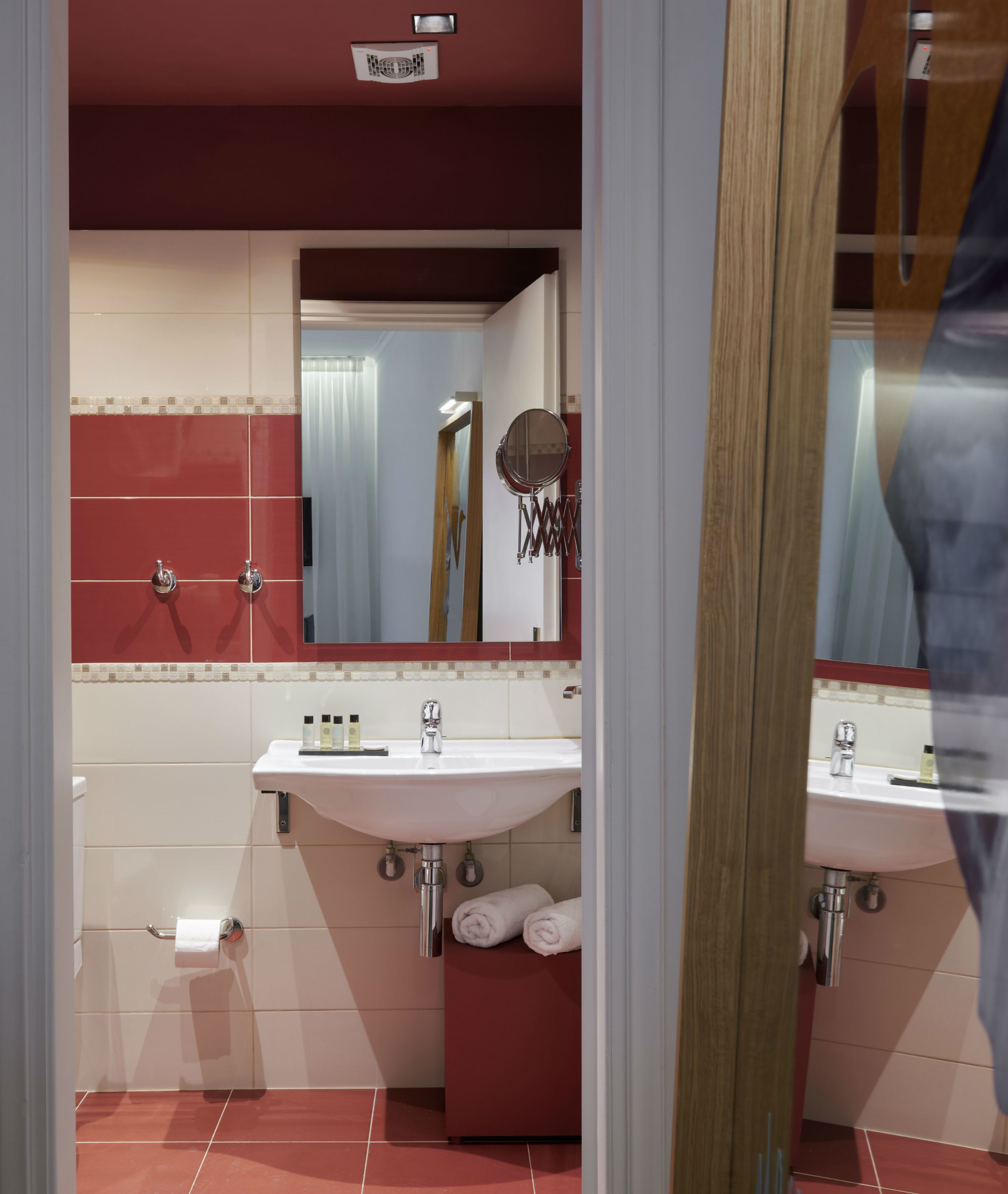 Un baño con pared de azulejos blancos y rojos, un lavabo blanco, un espejo y un inodoro.