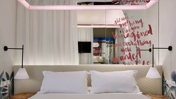 A modern bedroom with a bed, two bedside tables, a wall-mounted TV, and a decorative quote.