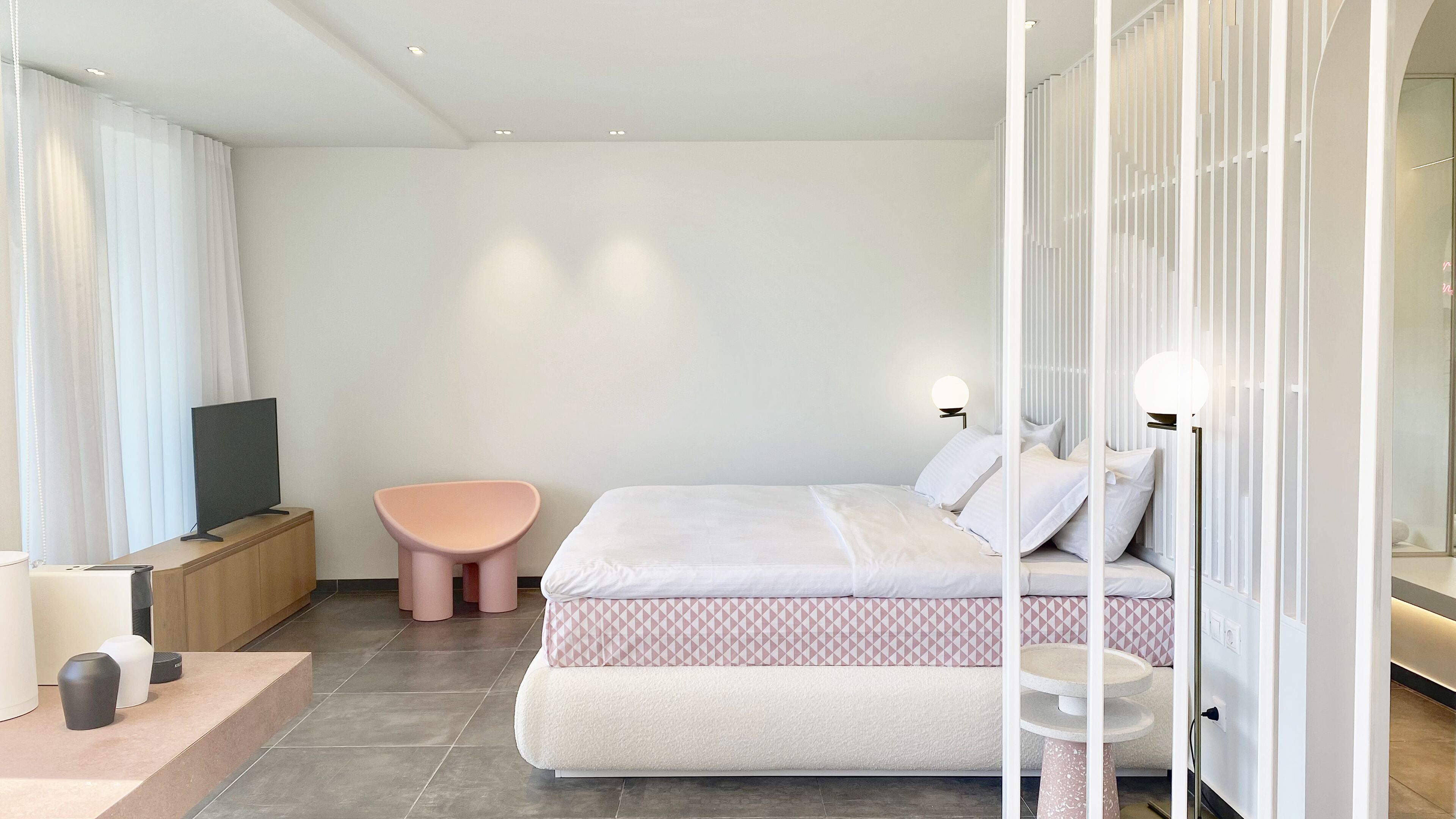 A modern bedroom with a bed, bedside tables, a TV, and a pink chair.
