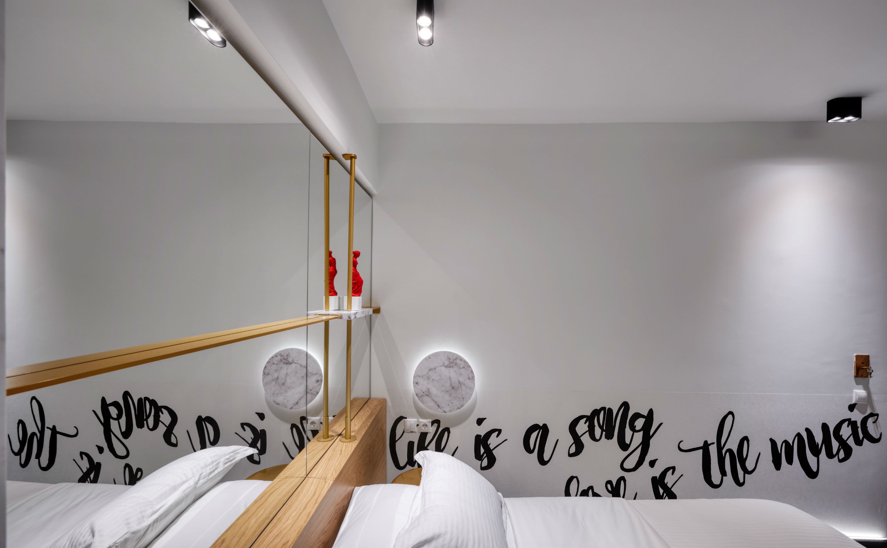 Un dormitorio moderno con estructura de cama de madera, ropa de cama blanca y una pared con citas motivacionales.