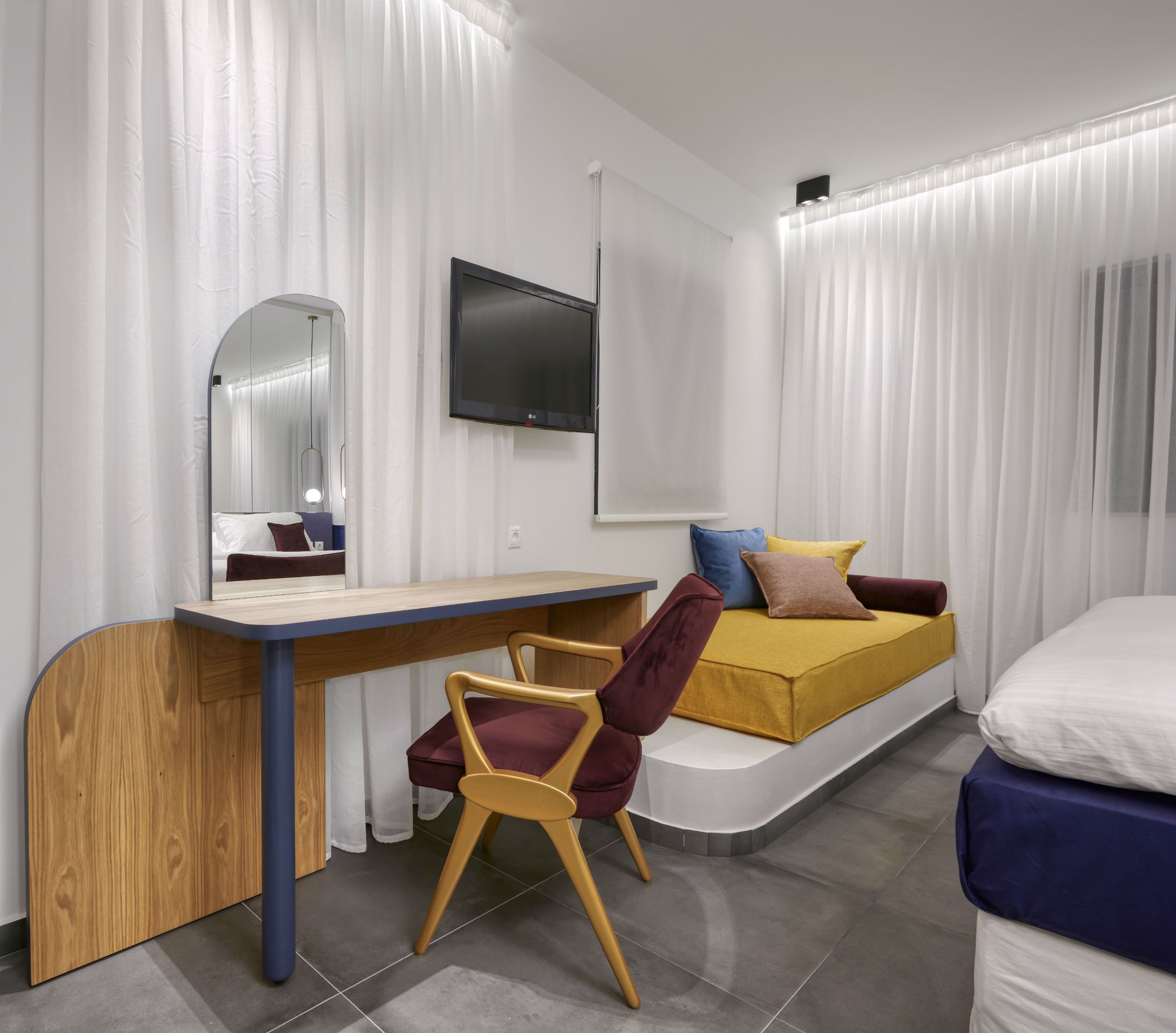 Une chambre moderne avec un bureau en bois, un canapé confortable, un lit et un téléviseur fixé au mur.