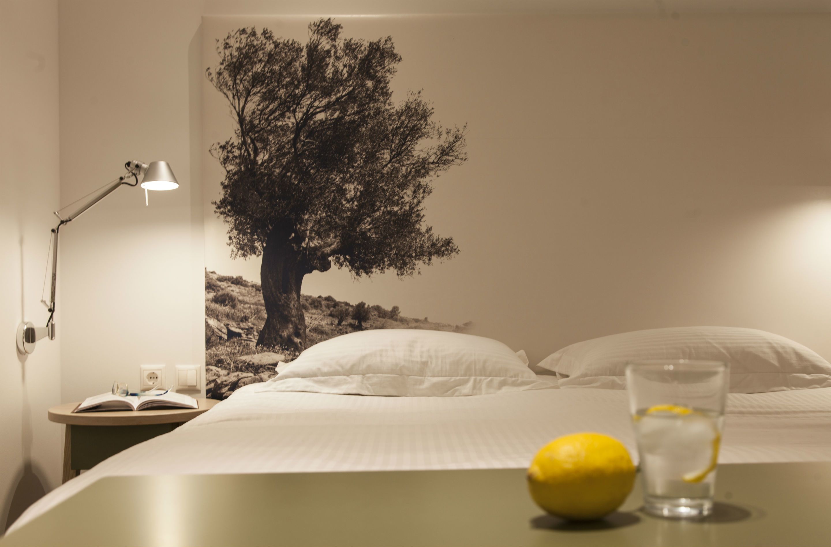 A bedroom with a bed, a nightstand with a lamp, a glass of water, and a lemon on the bedside table.