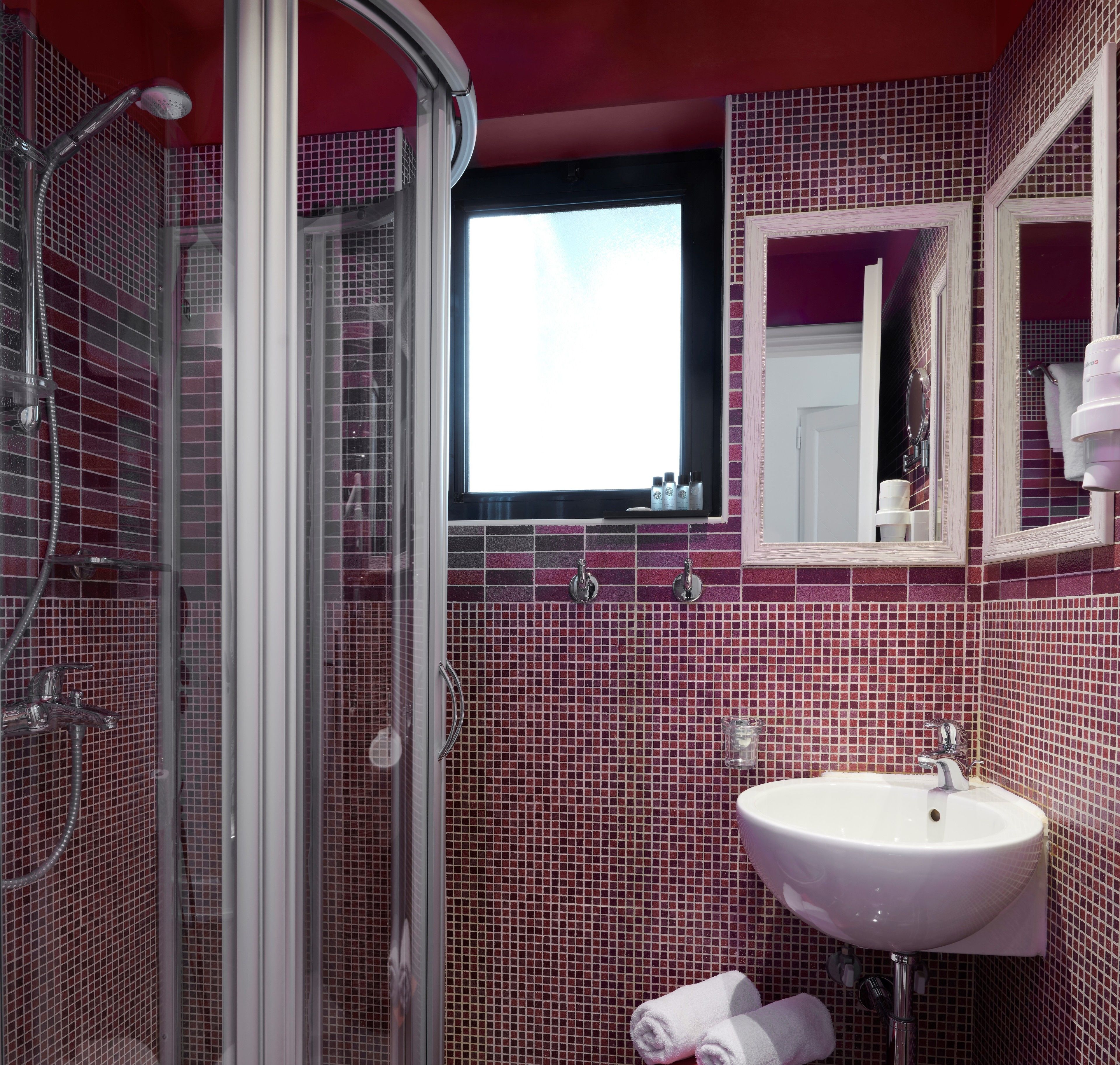 A bathroom with a glass shower enclosure, a sink, and a mirror.