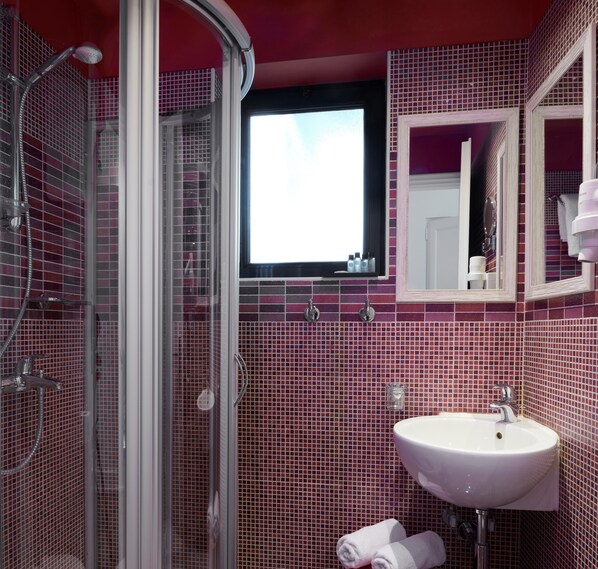 A bathroom with a glass shower enclosure, a sink, and a mirror.