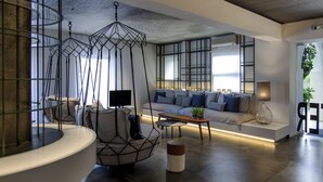 Una sala moderna con una silla colgante de diseño geométrico, un sofá con cojines, una mesa de centro y un televisor.