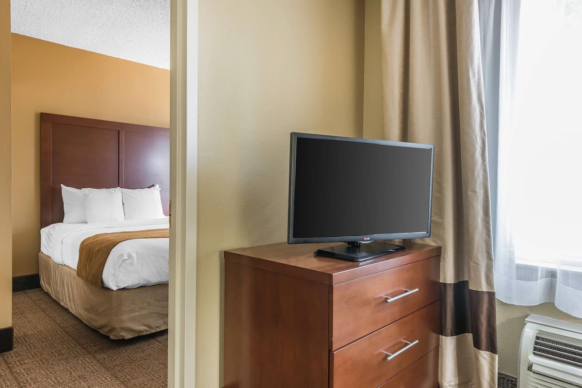 Una habitación de hotel con una cama, un televisor sobre una cómoda de madera y una ventana con cortinas.