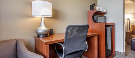 A hotel room with a desk, a chair, a lamp, a microwave, and a sofa.
