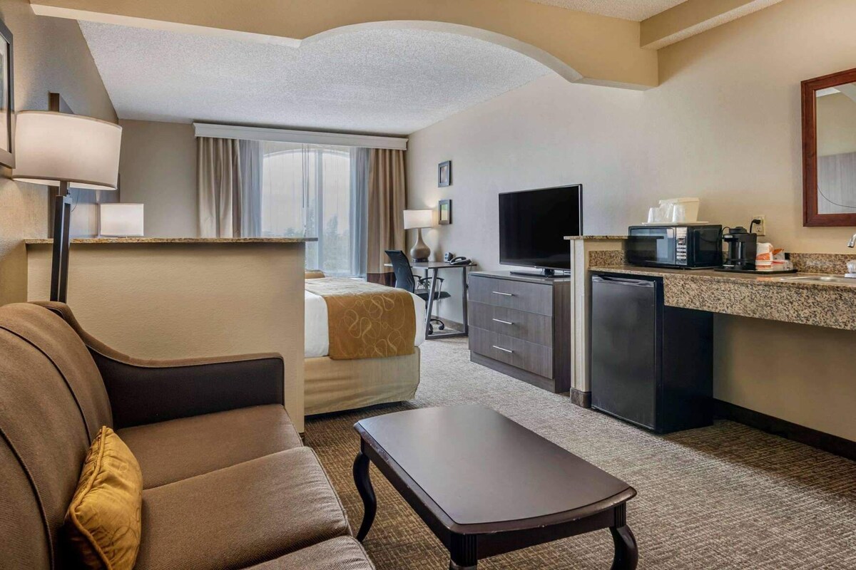 A hotel room with a bed, a desk, a television, a refrigerator, and a coffee maker.