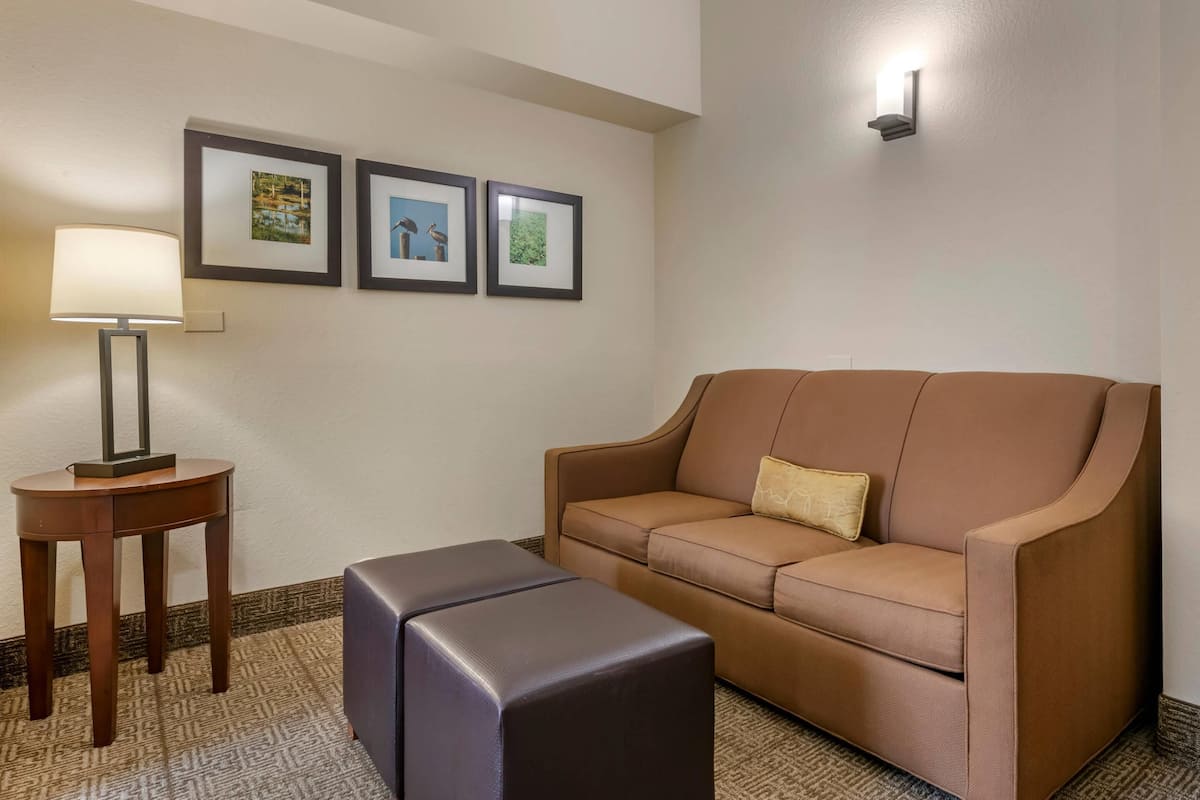Una habitación con un sofá de cuero marrón, un reposapiés a juego, una mesita de madera con una lámpara, y tres cuadros en la pared.