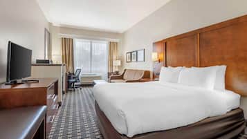 Een hotelkamer met een groot bed, een bureau met een televisie, een stoel en een raam met gordijnen.