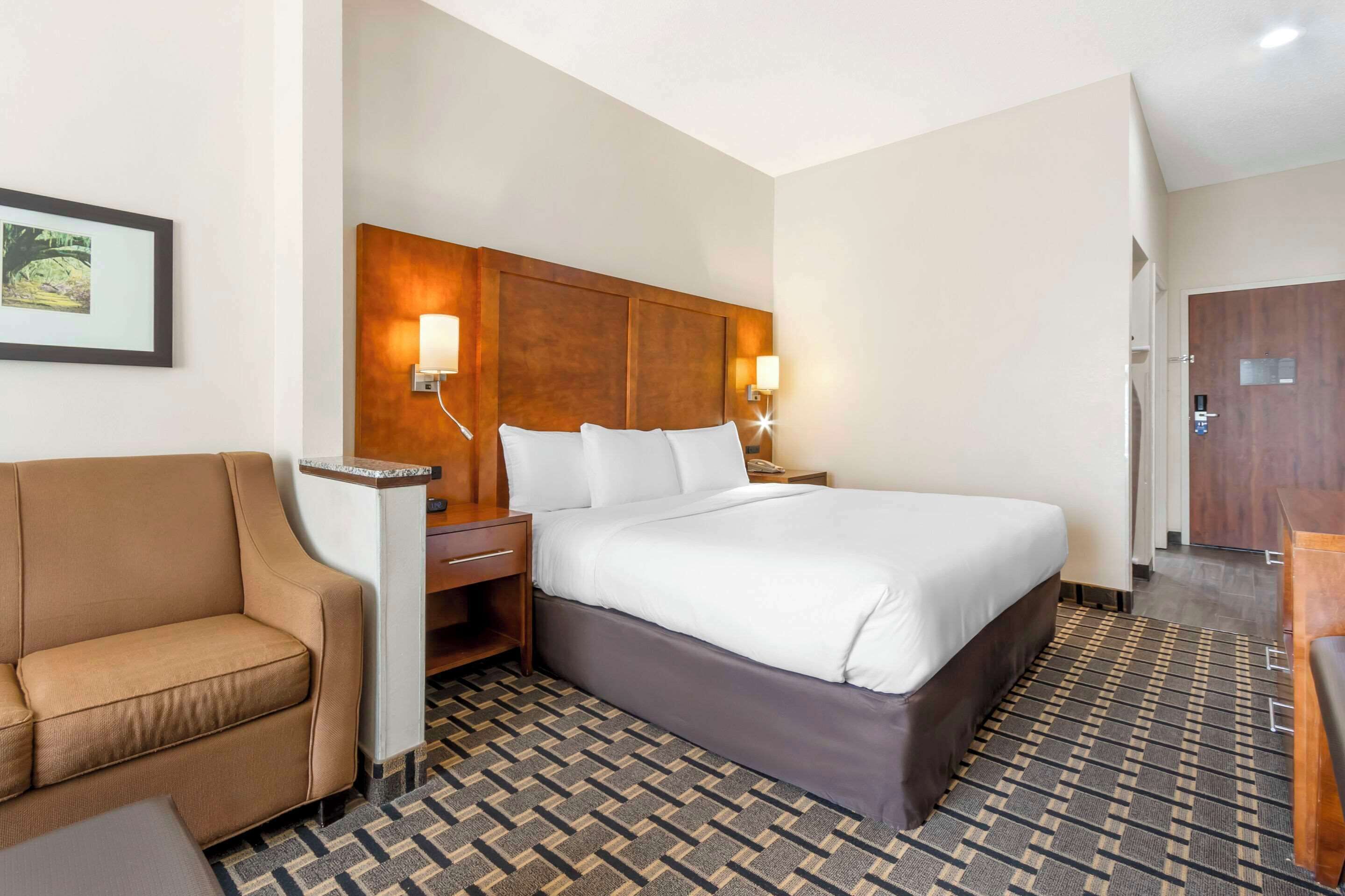 A hotel room with a large bed, a sofa, a nightstand, and a wall-mounted lamp.