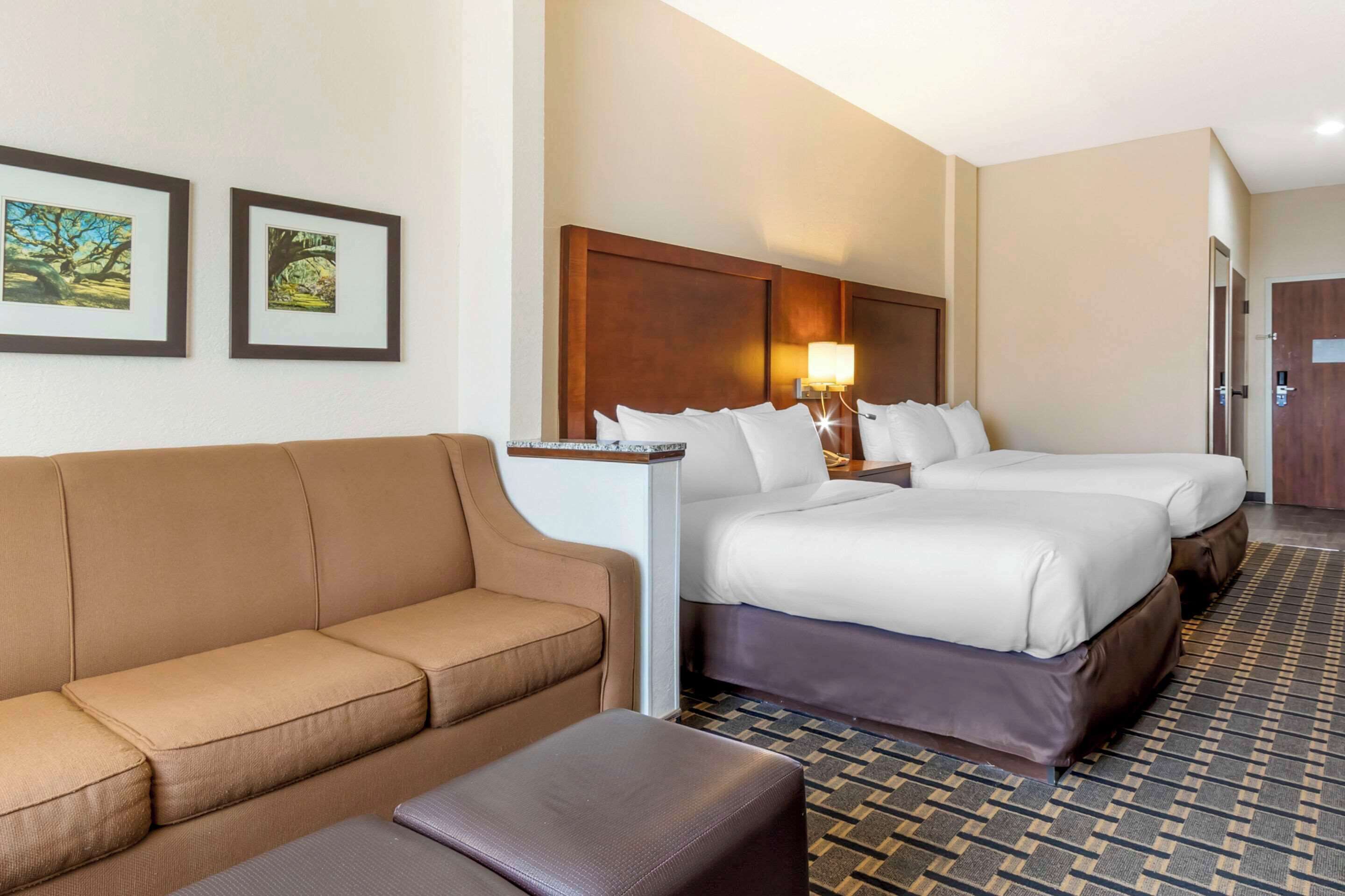 A hotel room with a sofa, a bed with two pillows, a nightstand with a lamp, and framed pictures on the wall.
