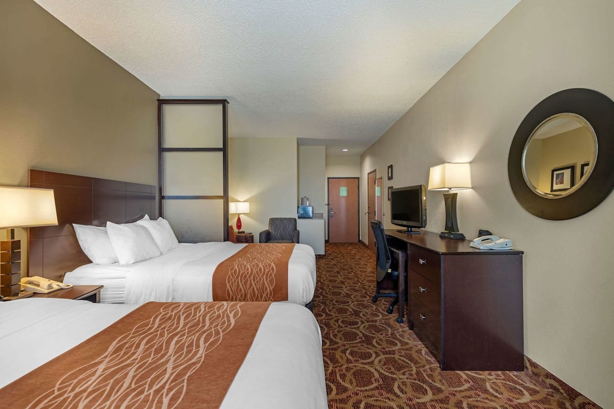 A hotel room with two beds, a desk with a computer, a chair, a desk lamp, a telephone, and a mirror.