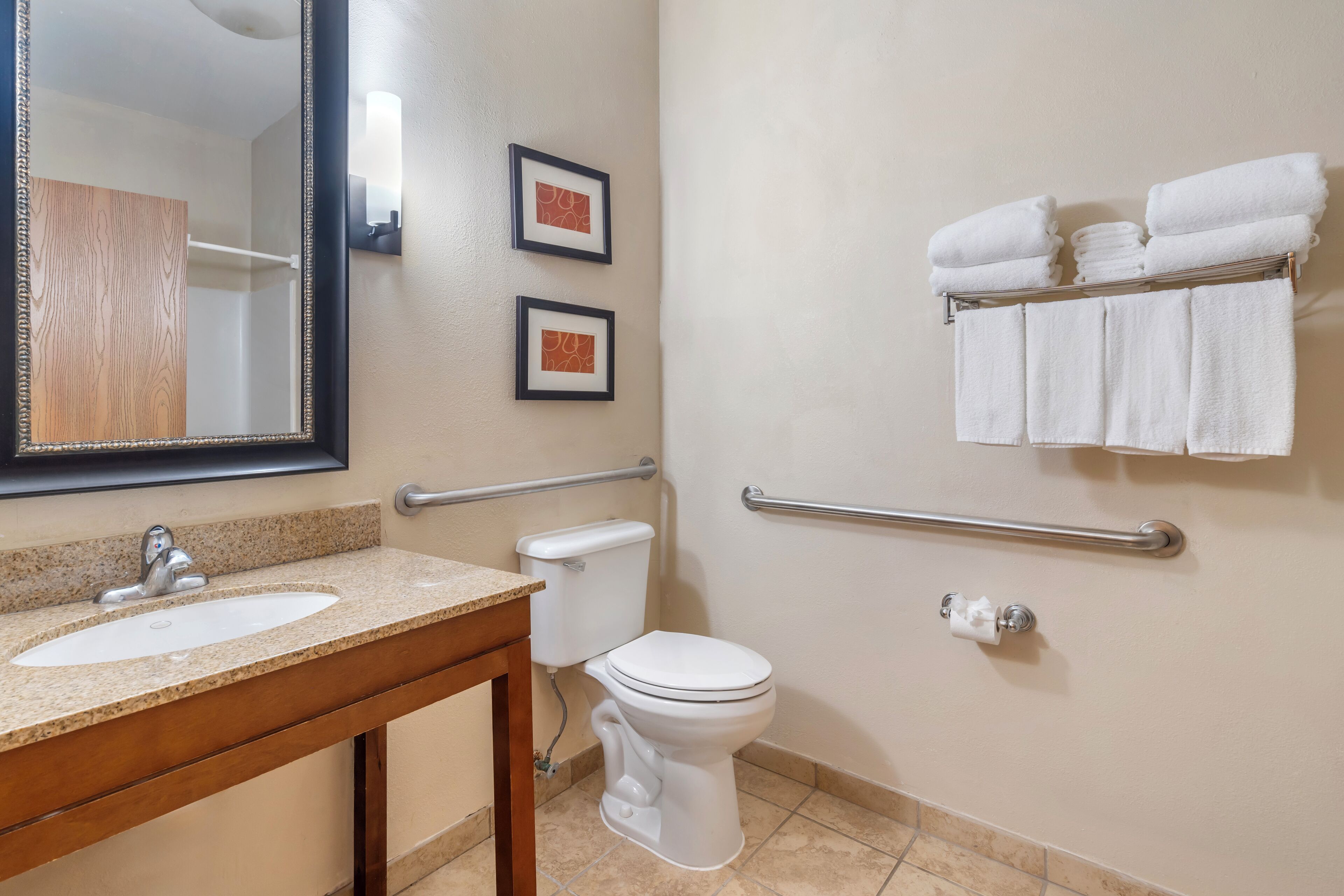 A bathroom with a sink, toilet, and handrails. There are framed pictures on the wall and towels on a rack.