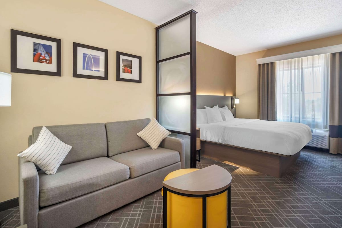 A hotel room with a sofa, a bed, a small table, and framed pictures on the wall.