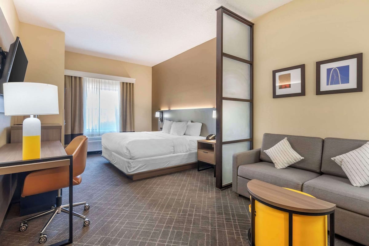 A hotel room with a bed, a desk with a chair, a sofa, and two framed pictures on the wall.