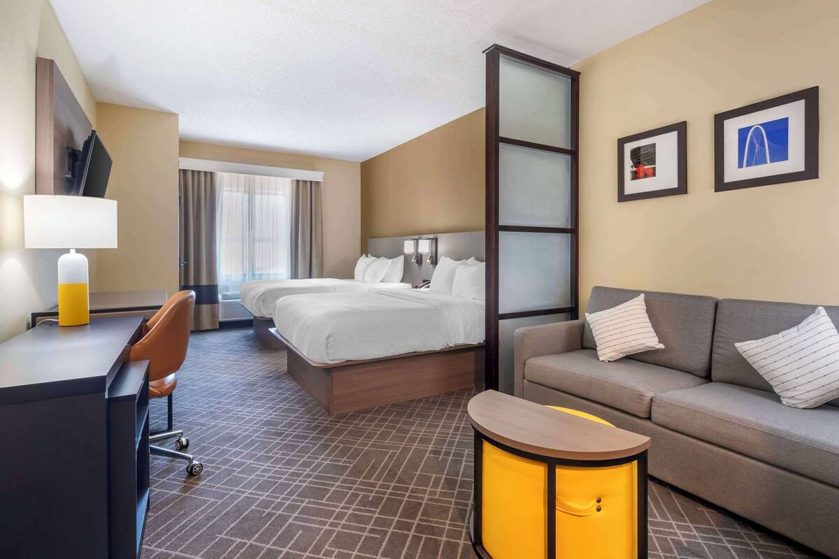 A hotel room with a bed, a sofa, a desk, and a lamp.