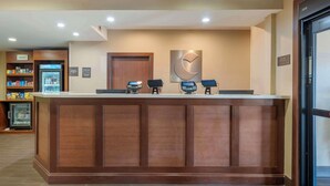 A reception desk with a wooden finish, a clock, and a refrigerator stocked with beverages.