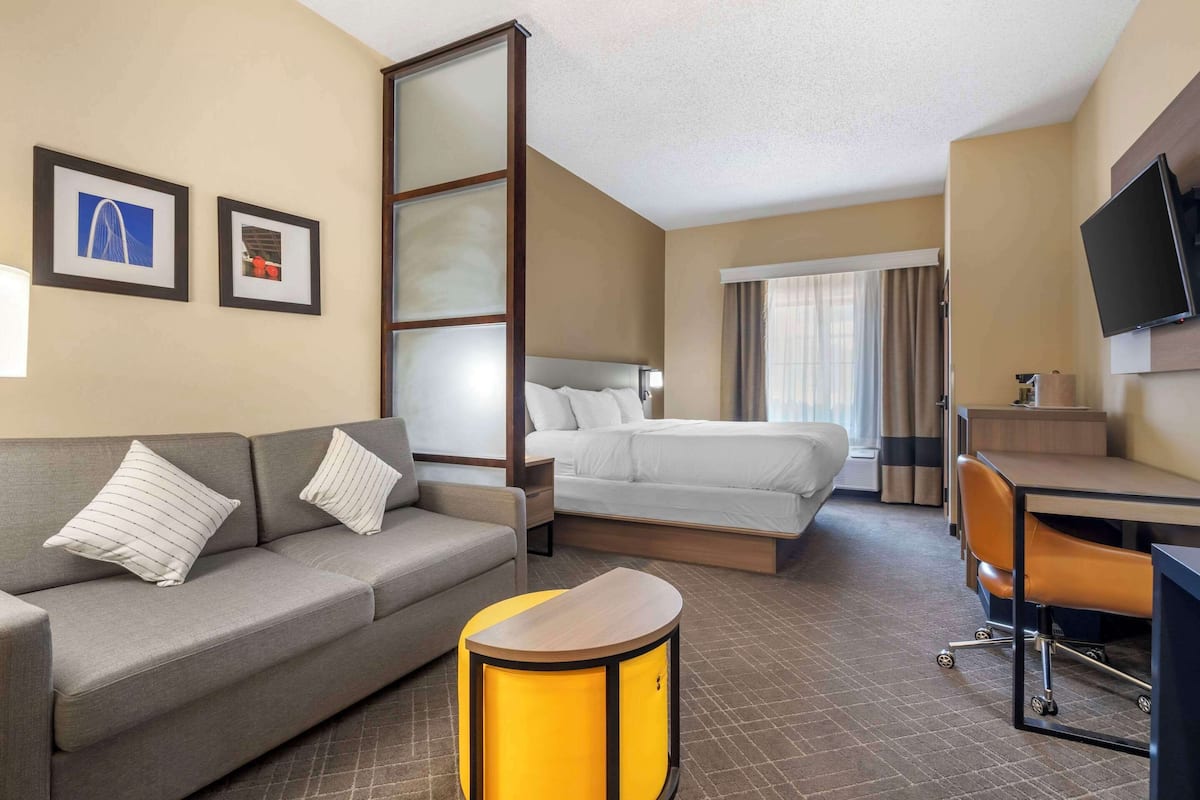 A hotel room with a sofa, a bed, a desk, a chair, a TV, and two framed pictures on the wall.