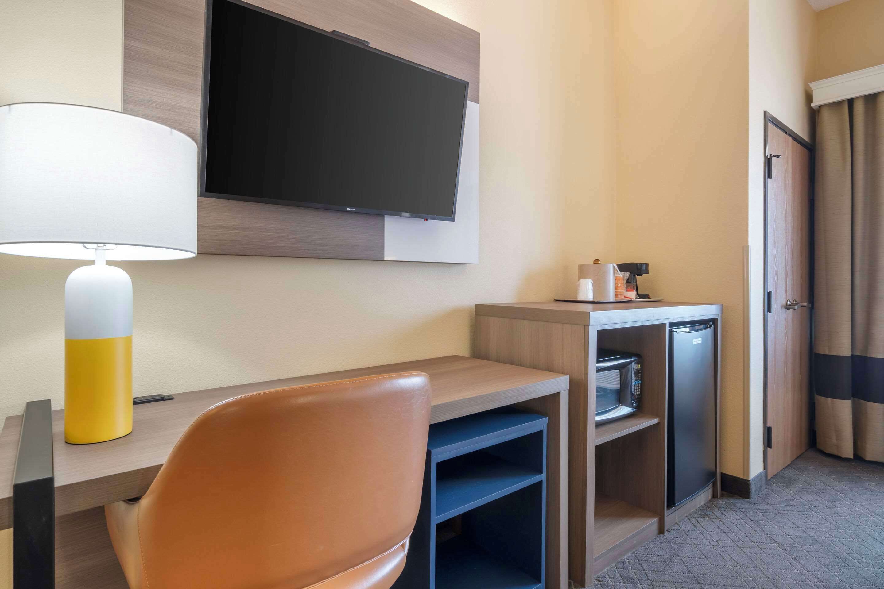 Une chambre d’hôtel équipée d’un bureau, d’une chaise, d’un téléviseur fixé au mur, d’un four à micro-ondes et d’un réfrigérateur.