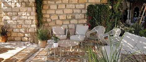Une terrasse aux murs de pierre, dotée de meubles d’extérieur, de plantes en pot et d’un tapis à motifs.