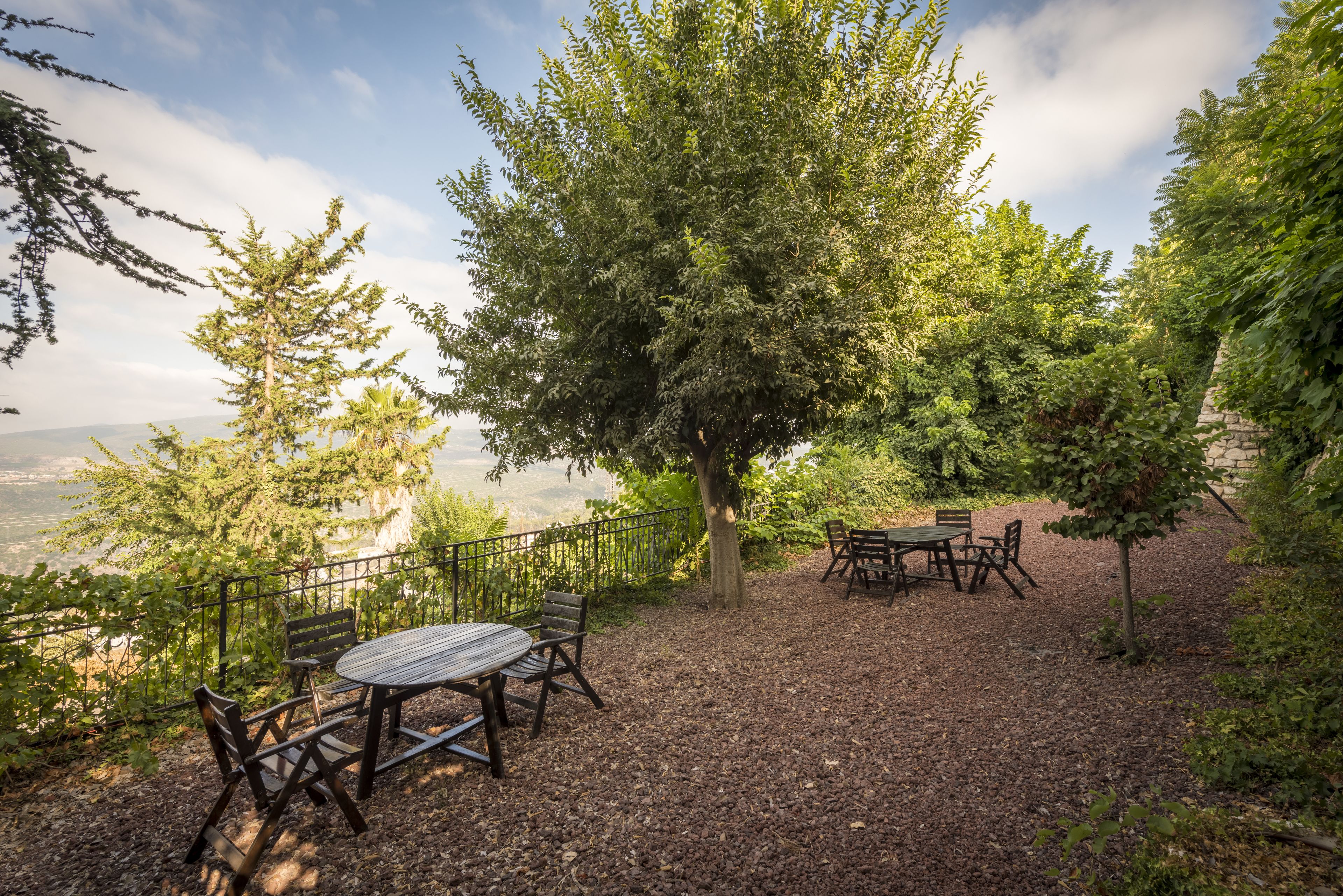 An outdoor seating area with a table and chairs, surrounded by trees and a view of the landscape.