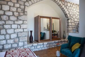 Una habitación con pared de piedra, un espejo grande, un sillón color turquesa y un armario de madera.