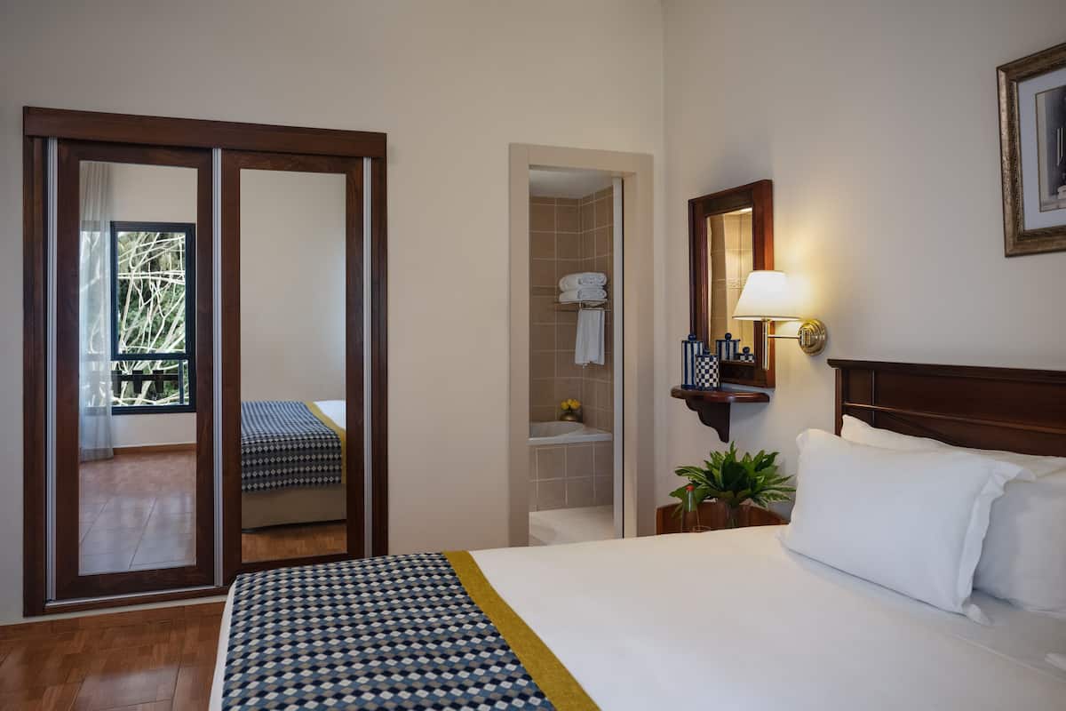 A hotel room with a bed, a bathroom, a sliding door to a balcony, and a nightstand with a lamp.