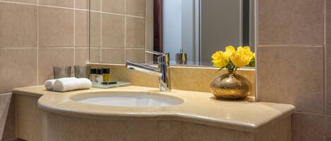 Un bagno con un lavandino color beige, uno specchio e un vaso con fiori gialli.