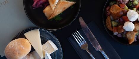 Un tavolo apparecchiato con diversi piatti, tra cui verdure, una zuppa e formaggio. Si vedono anche due bicchieri di vino, un coltello e una forchetta.