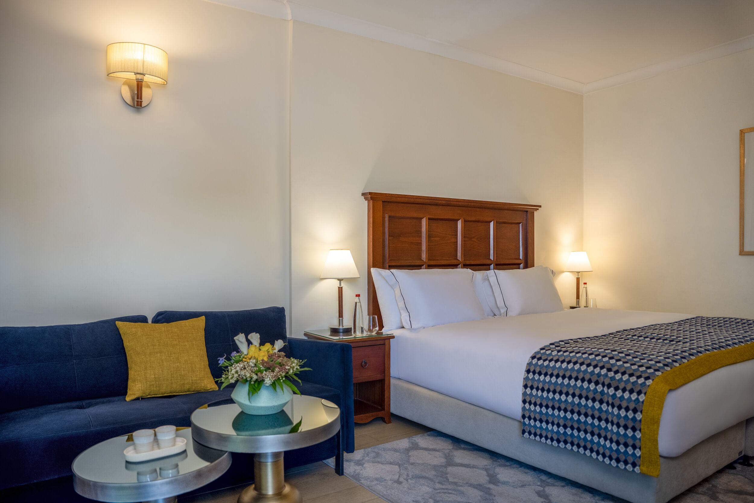 A hotel room with a bed, a sofa, a nightstand, and a lamp.