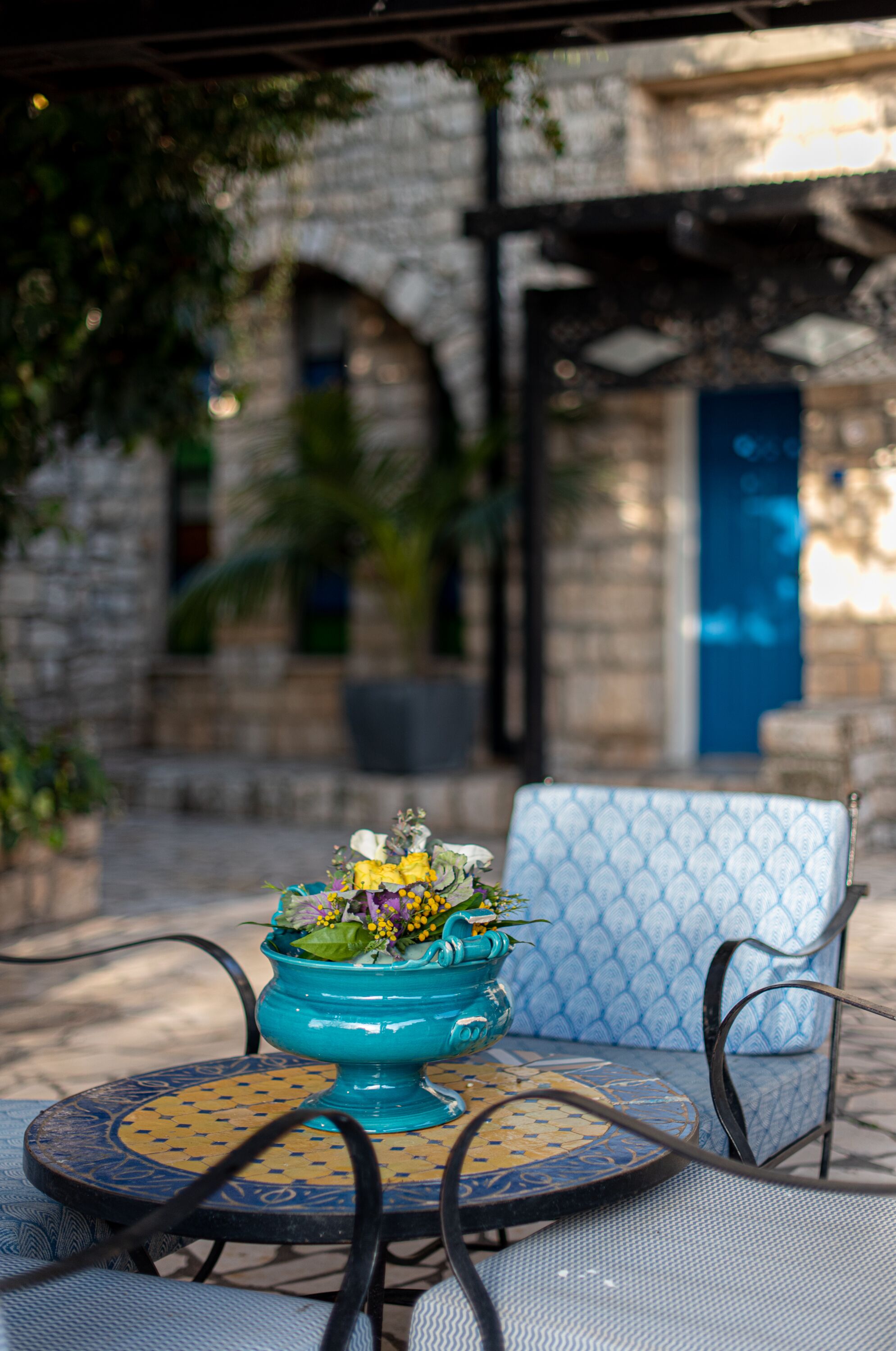 A table with a blue patterned tablecloth and a turquoise vase with flowers.