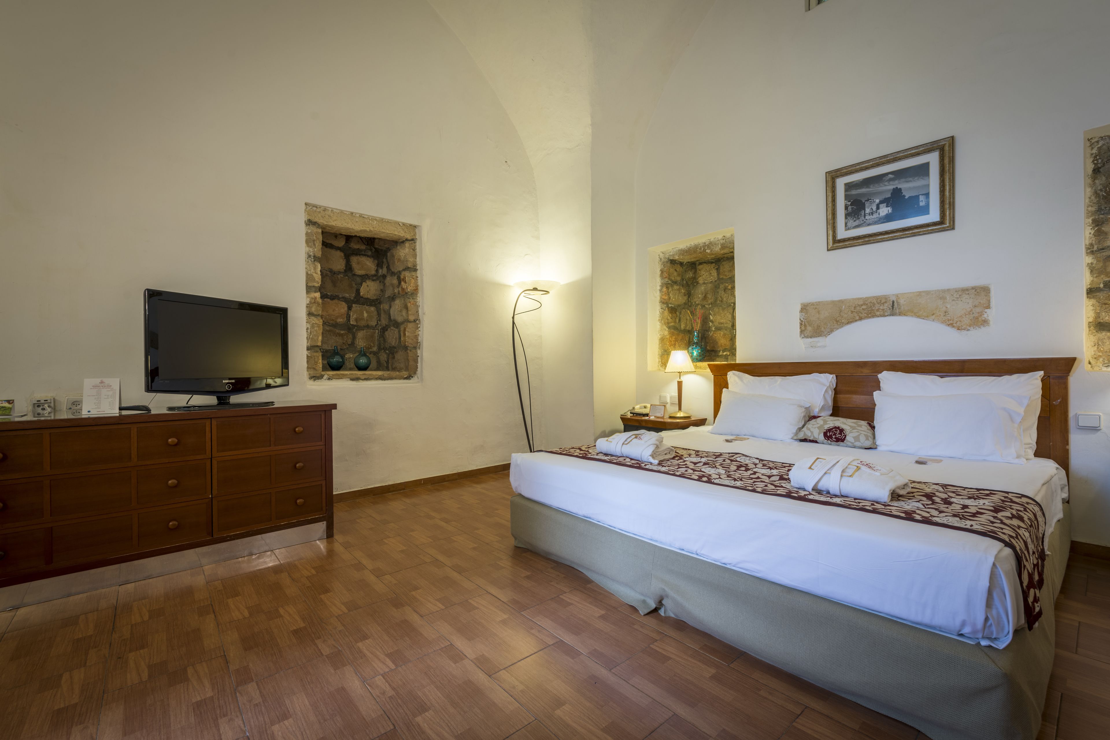 A bedroom with a bed, a TV, a dresser, and a lamp.