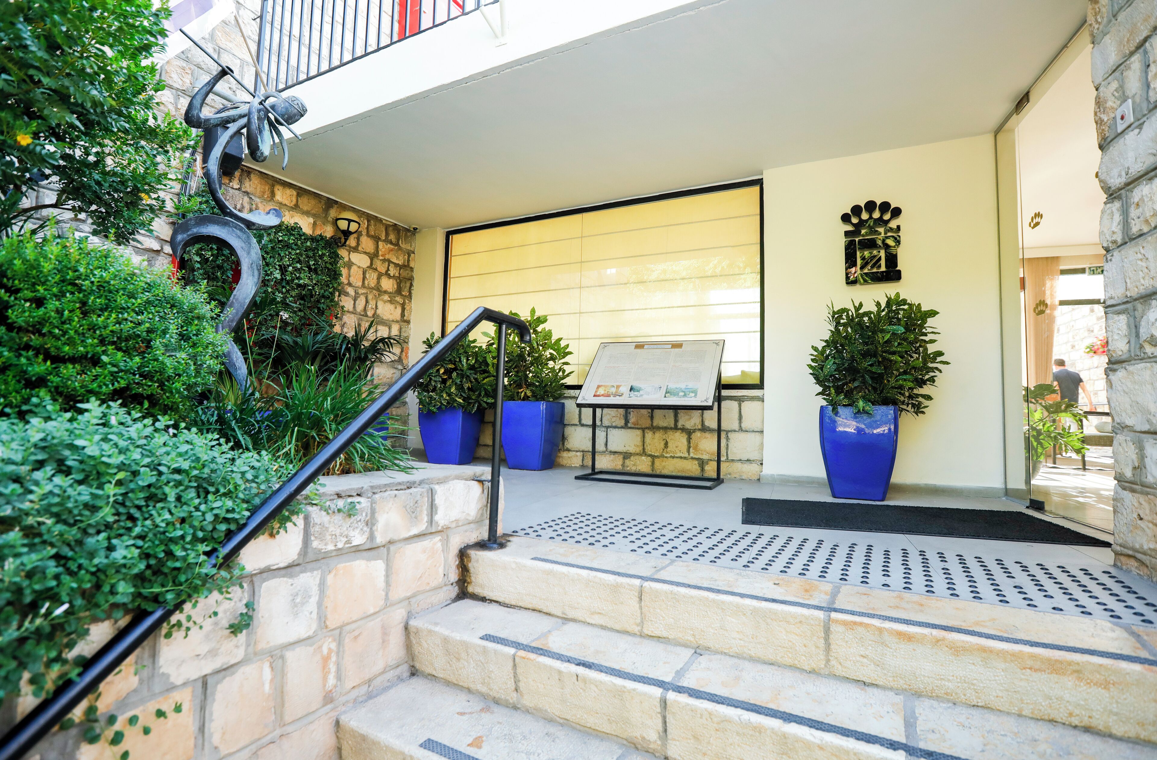 A hotel entrance with stone steps, a metal handrail, and potted plants.