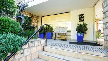 A hotel entrance with stone steps, a metal handrail, and potted plants.