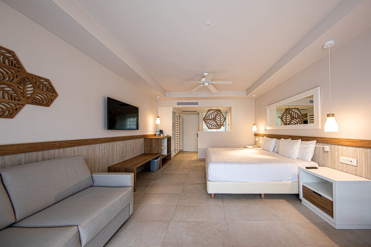 Ein Hotelzimmer mit Sofa, Bett, Fernseher, Deckenventilator und einem Wandbild.