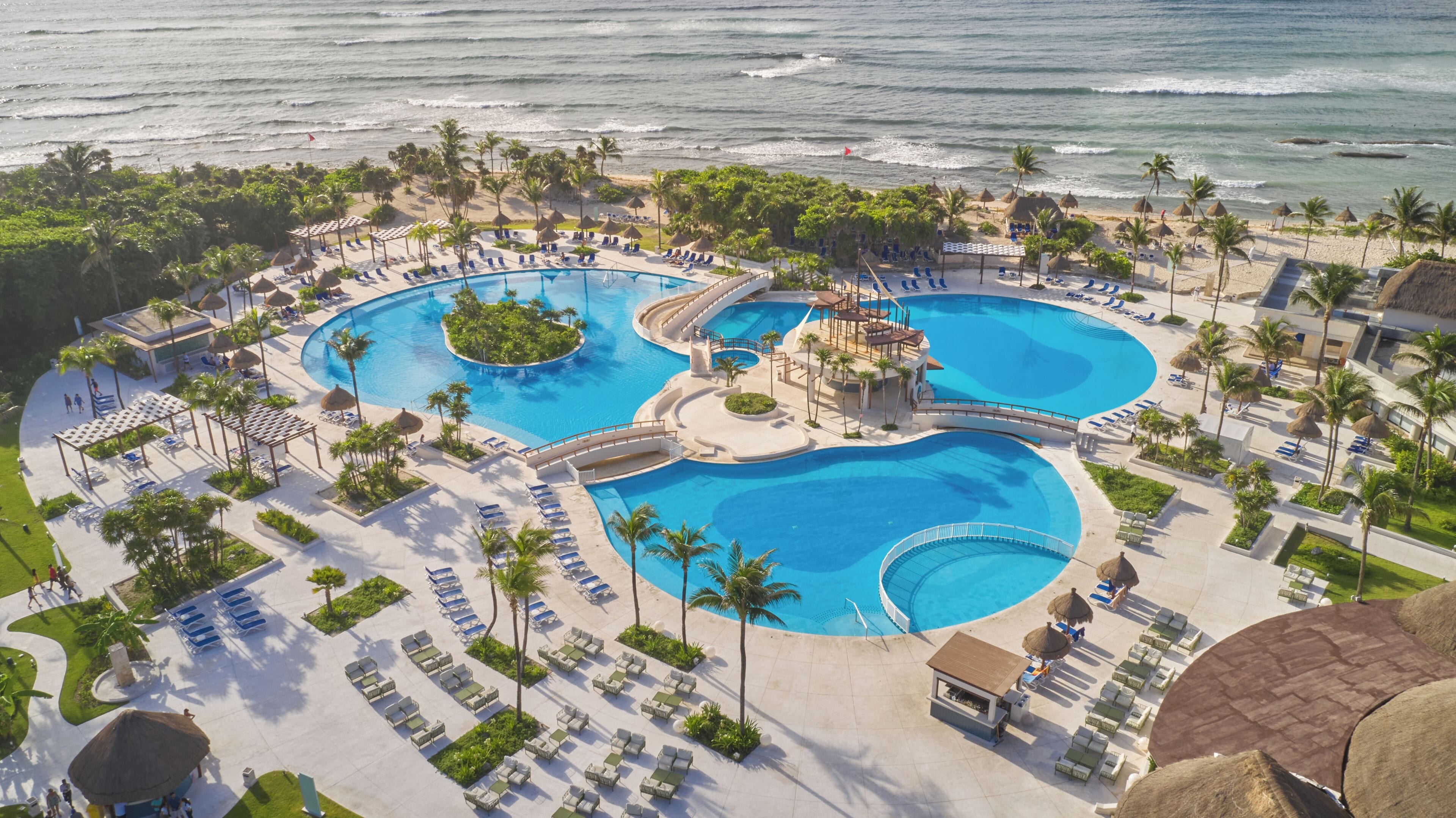 A resort with a large central pool, smaller surrounding pools, and a beach area.