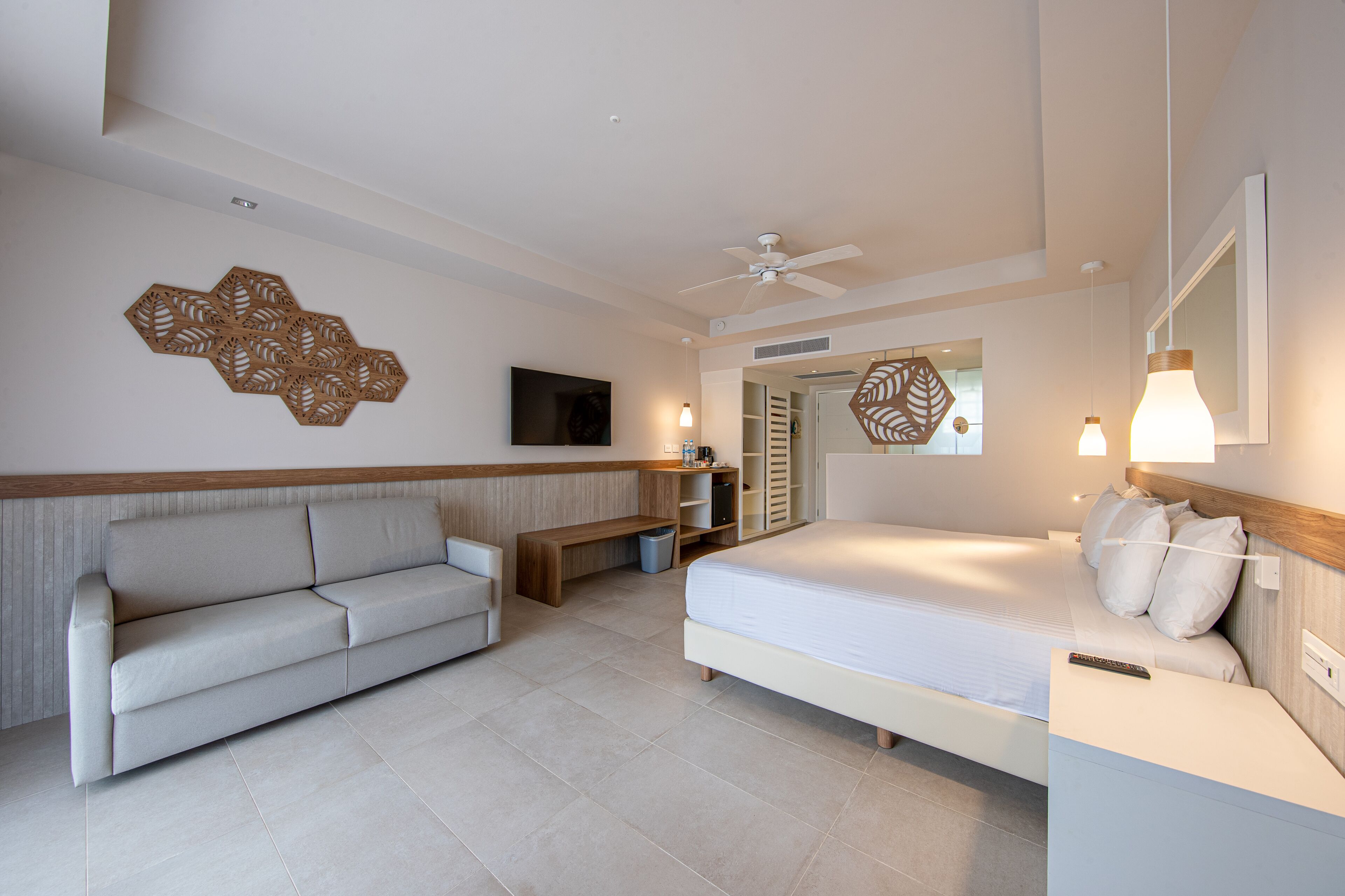 A modern hotel room with a bed, a sofa, a TV, and a ceiling fan.