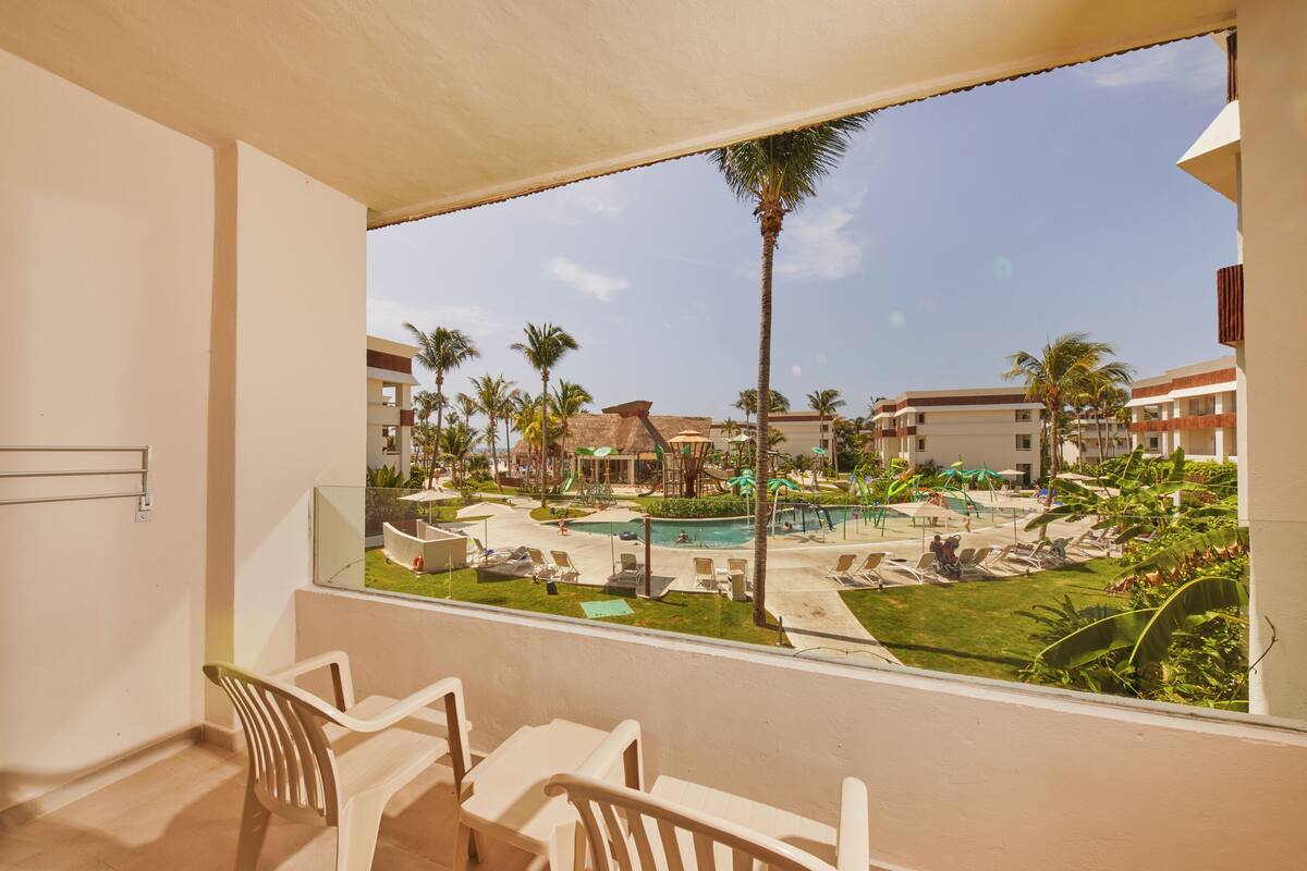 A balcony with a view of a pool area, including lounge chairs and palm trees.