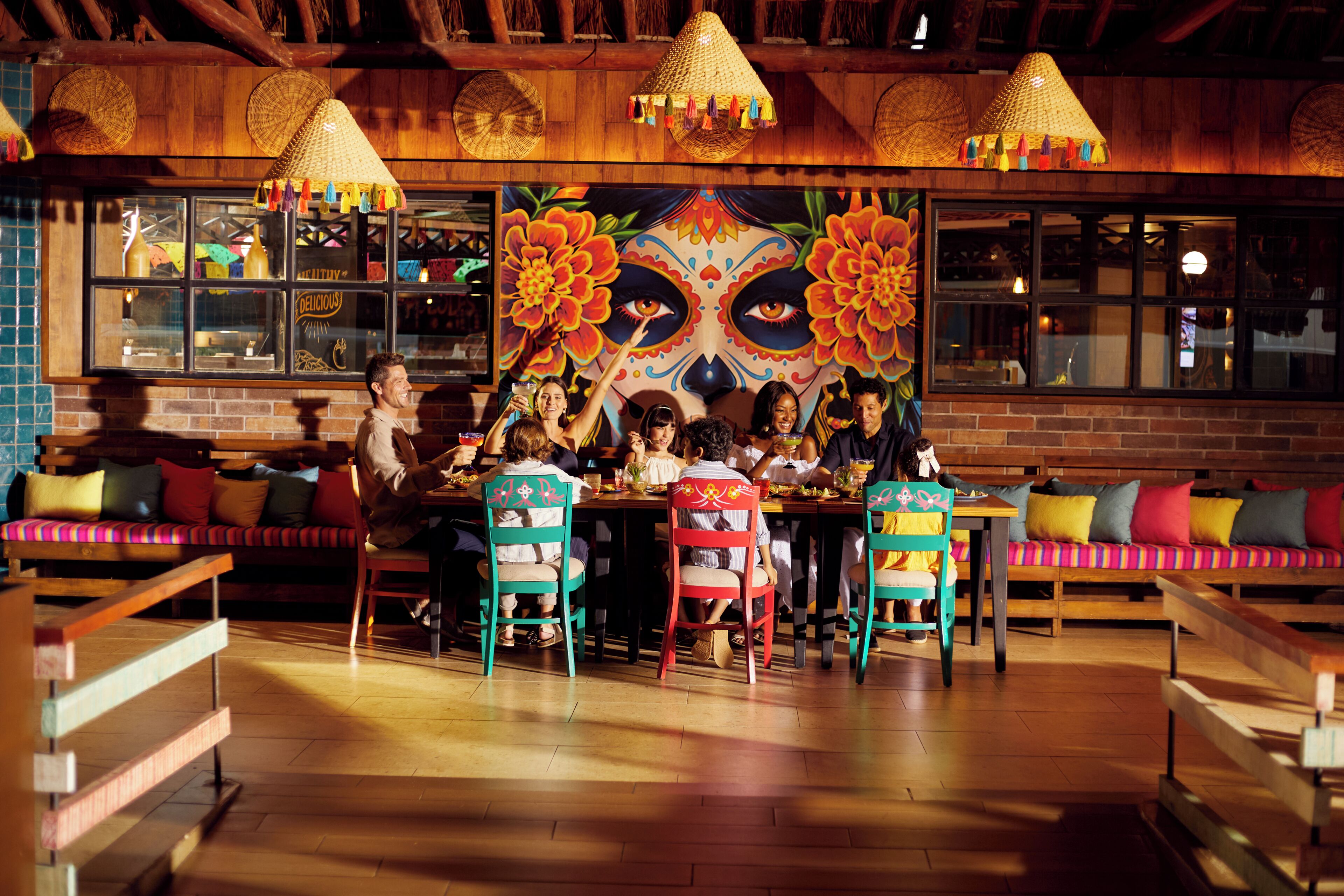 A restaurant with wooden furniture, colorful chairs, and a large mural with floral patterns.