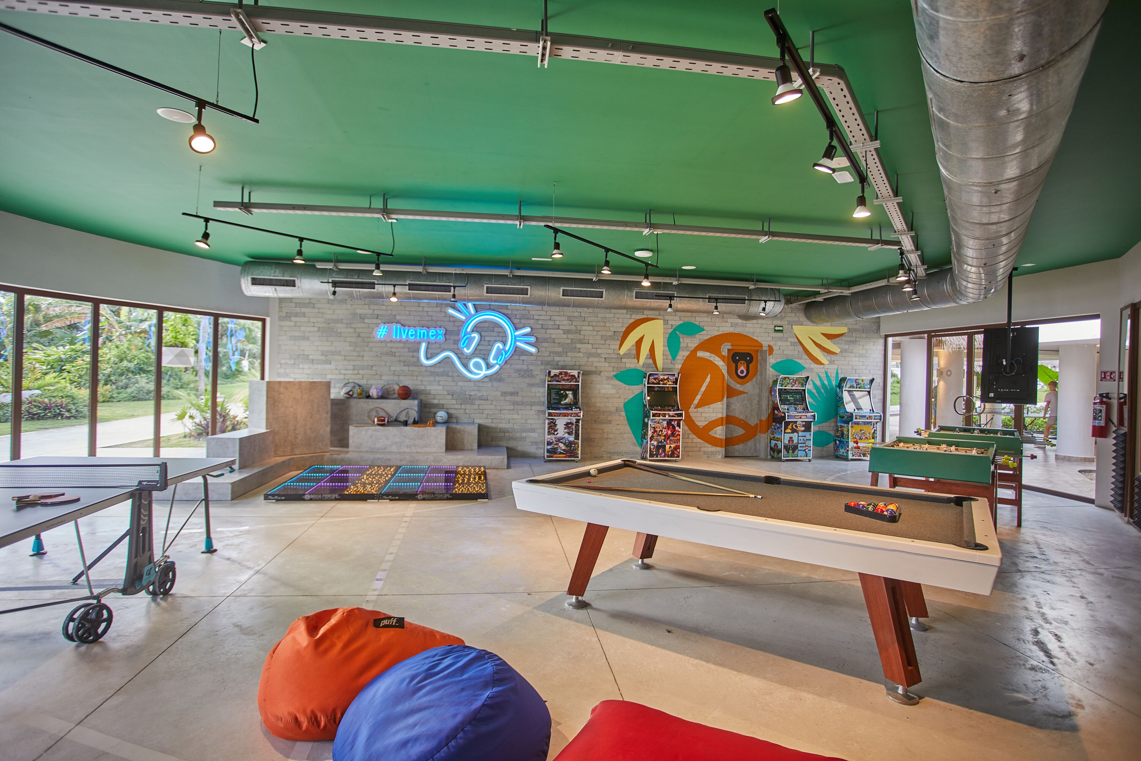 A recreational area with a pool table, bean bags, and a neon sign.
