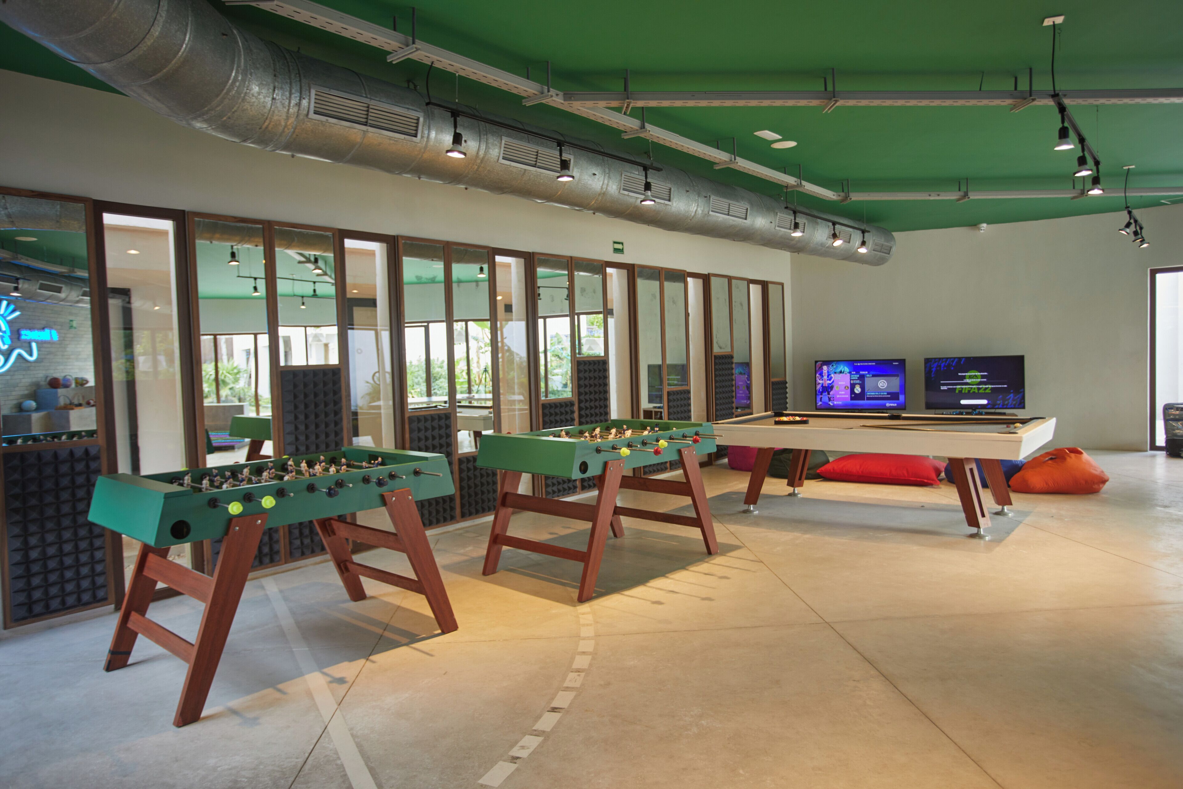 A room with two foosball tables, a pool table, and a television displaying a game.