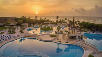 Un resort con una piscina grande, tumbonas y vista al océano al atardecer.