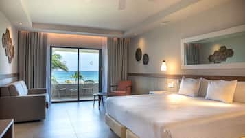 Habitación de hotel con una cama grande, un sofá, una silla, una mesita y un balcón con vista al océano.