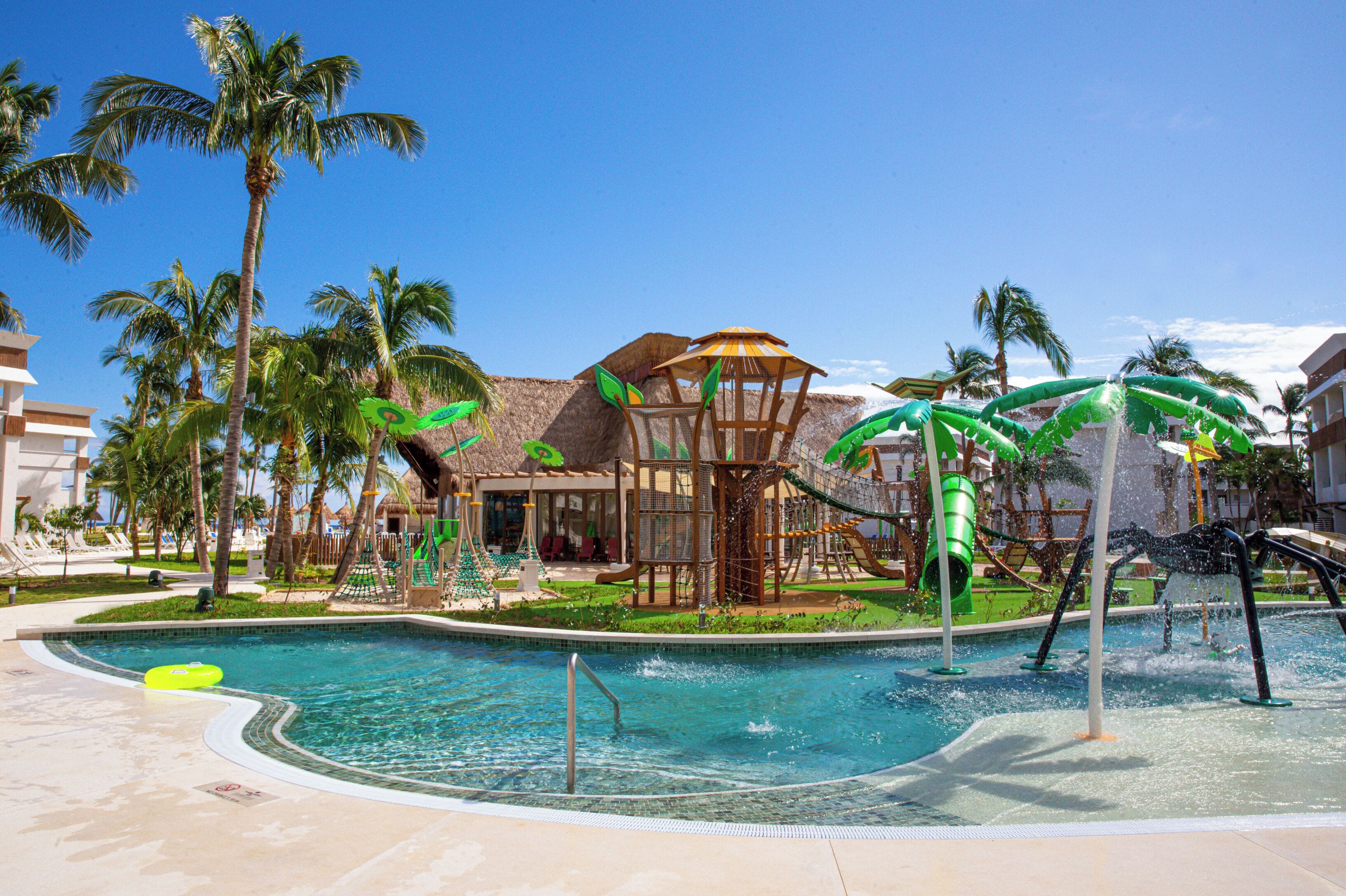 A pool area with a water slide, palm trees, and a building with a thatched roof.