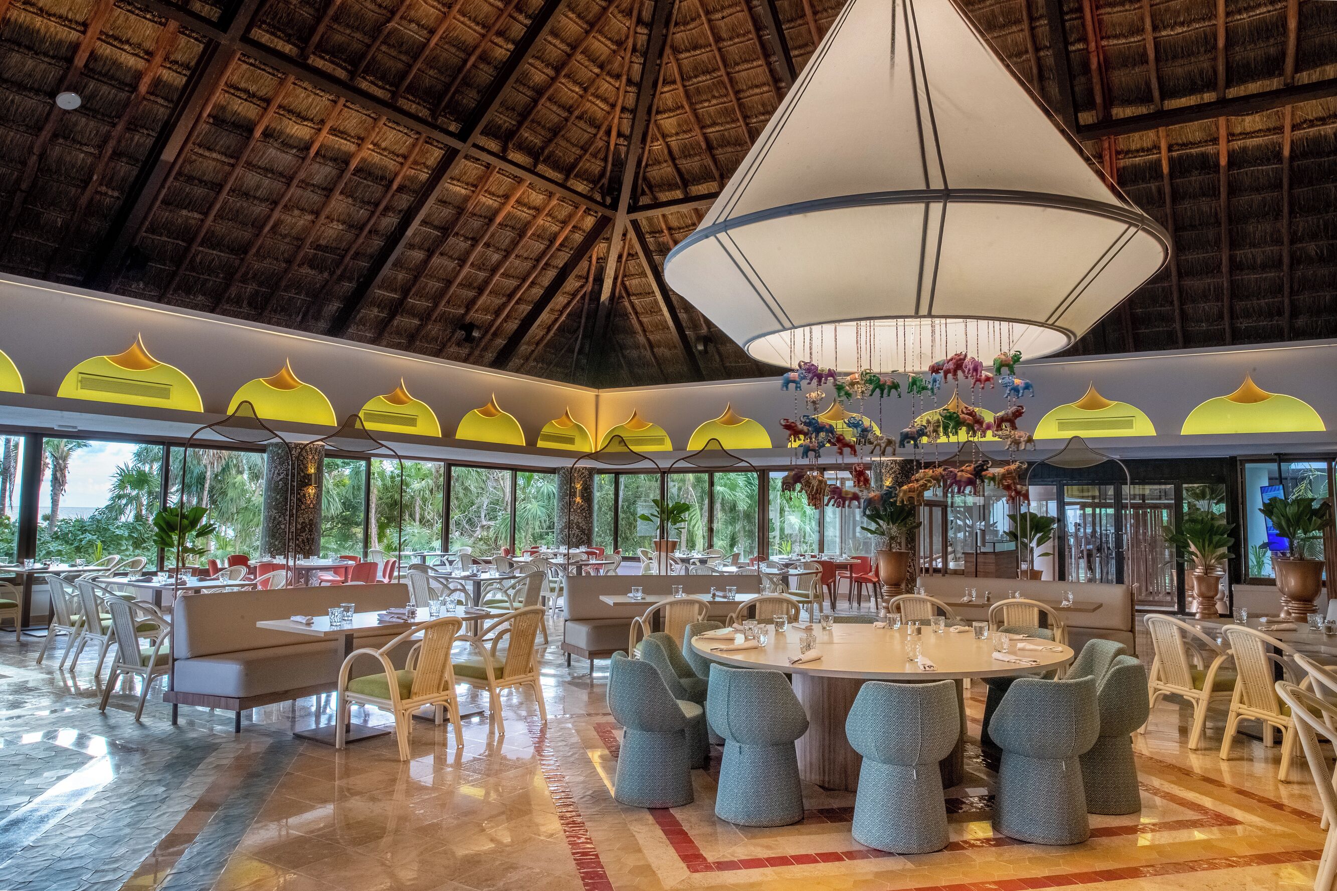 A spacious dining area with round tables, cushioned seating, and a large chandelier.