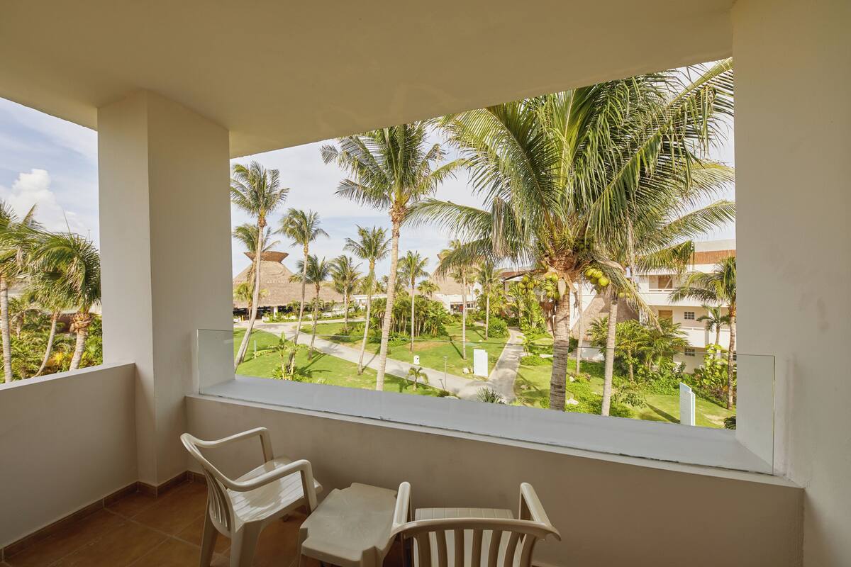 A balcony with two chairs and a table, overlooking a well-maintained garden with palm trees and a pathway.