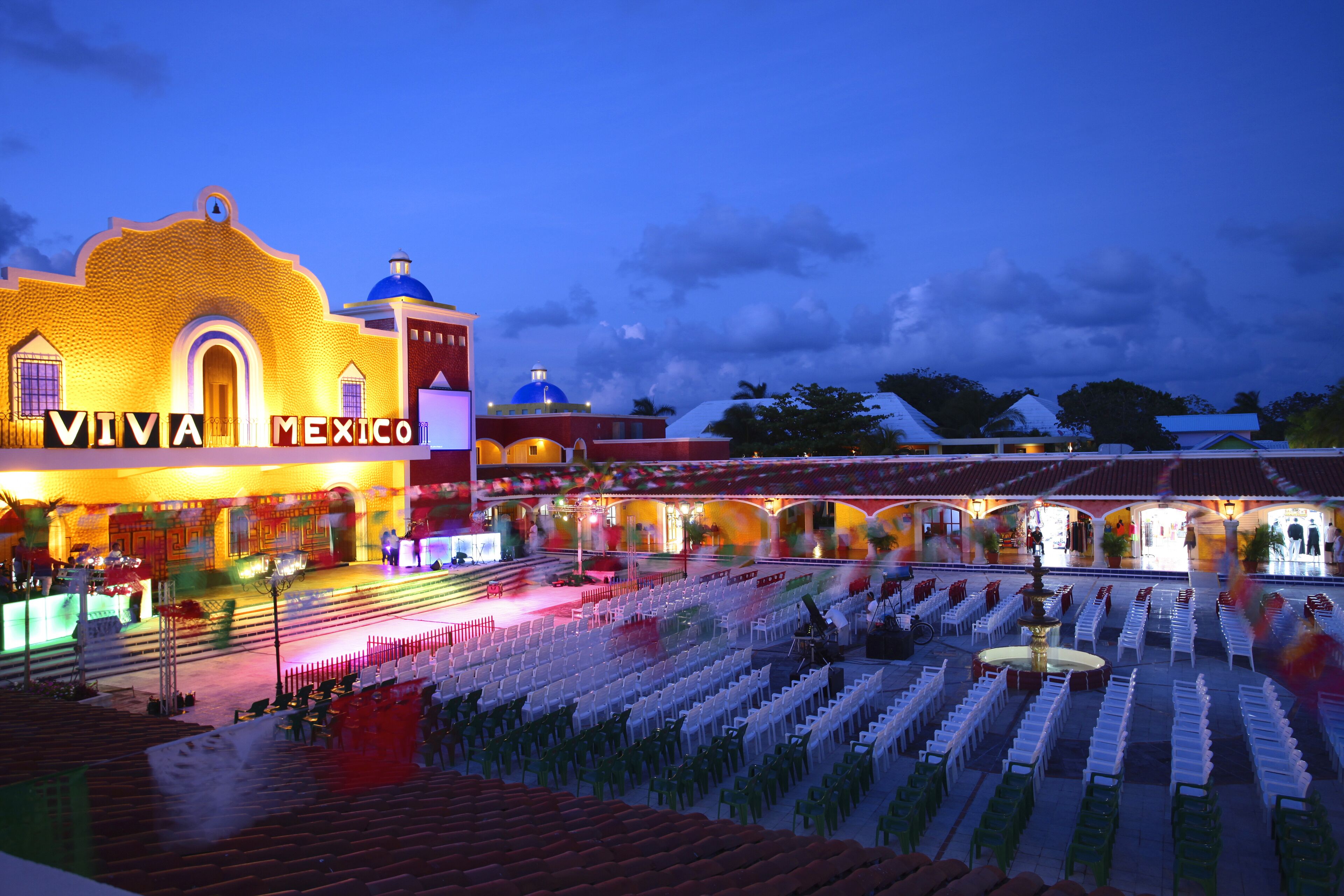 Un espacio para eventos con un escenario y filas de sillas, con la leyenda "VIVA MEXICO", lo que sugiere un lugar para una presentación o espectáculo.