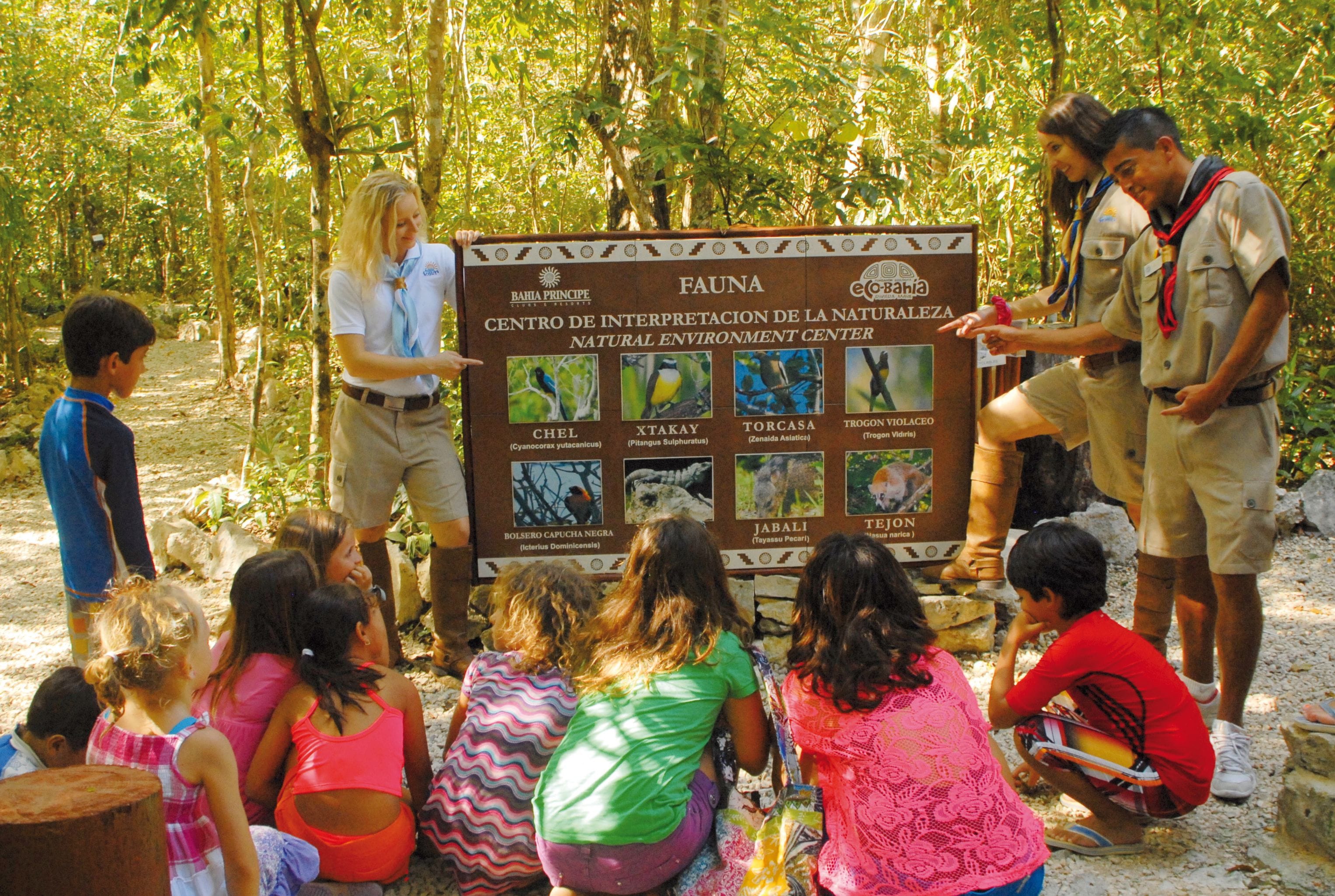 A group of people gathered around a signboard in a forested area, with a natural environment center sign.