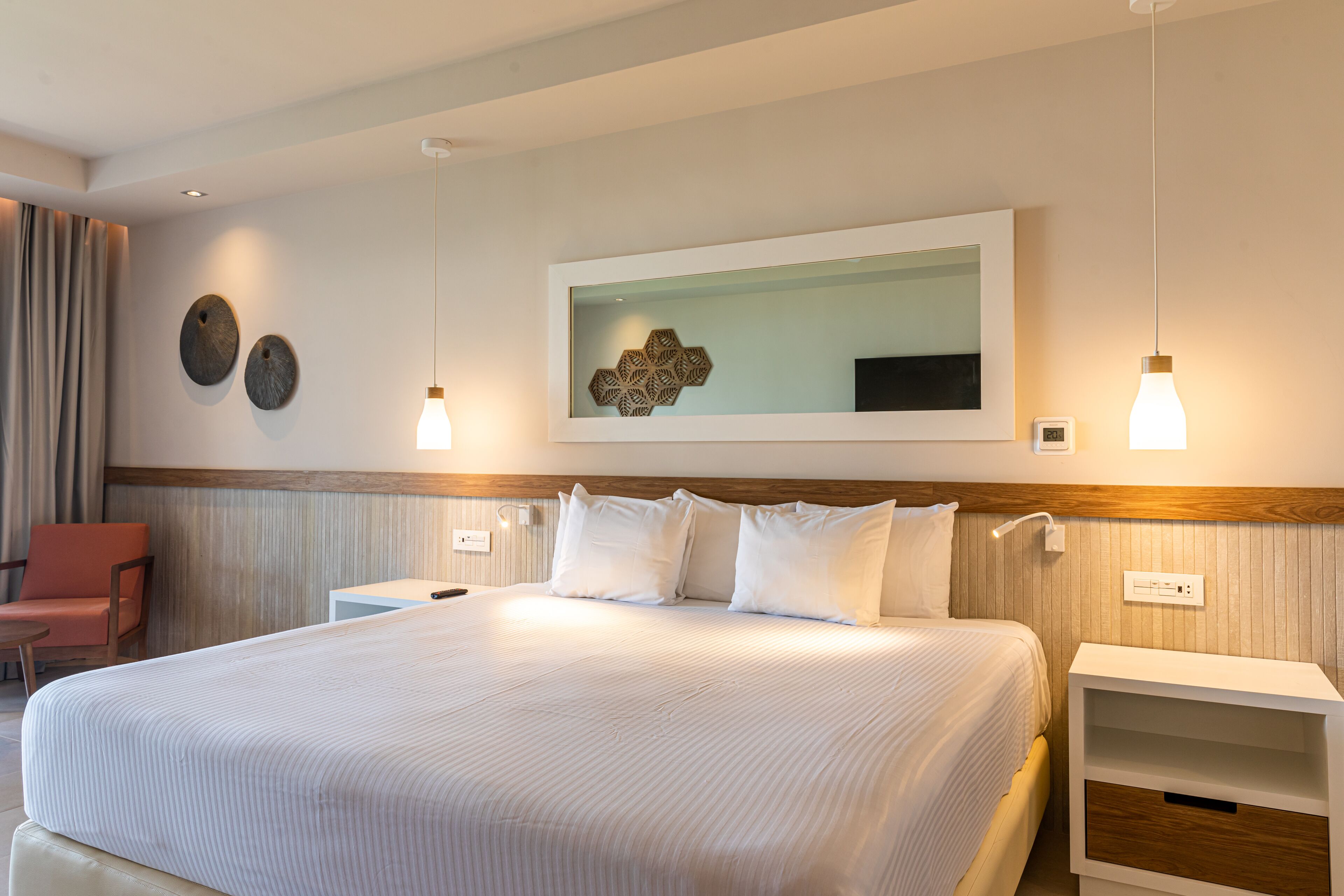 A hotel room with a large bed, bedside tables, a chair, and a wall-mounted artwork.